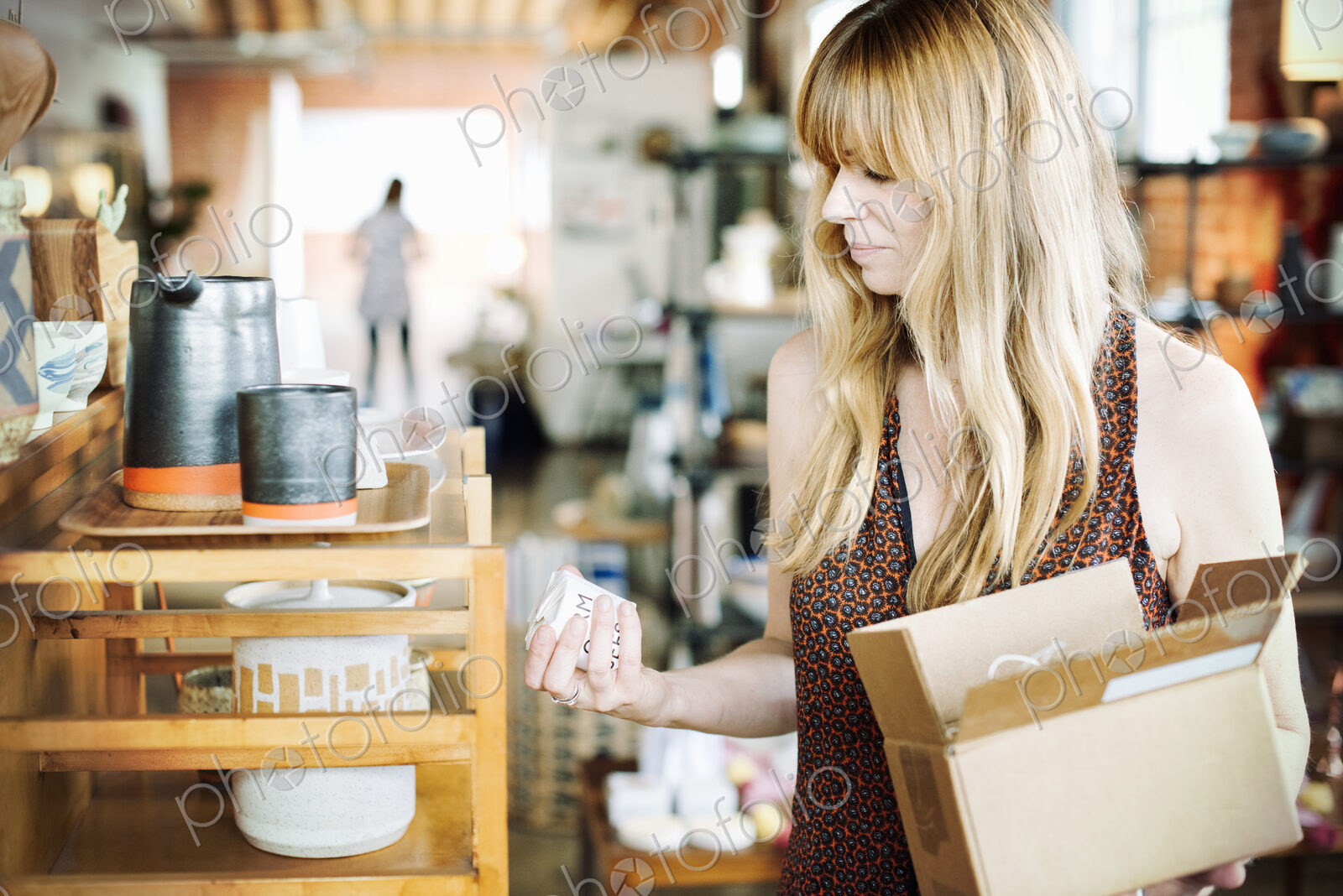 Woman in a shop, holding a small cardboard box with merchandise.