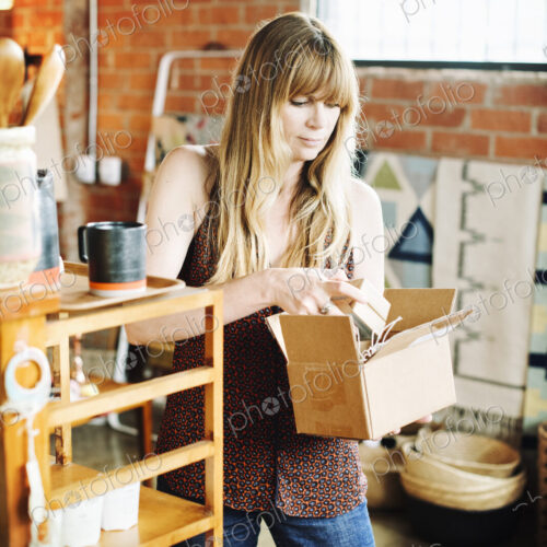Woman in a shop, holding a small cardboard box with merchandise.