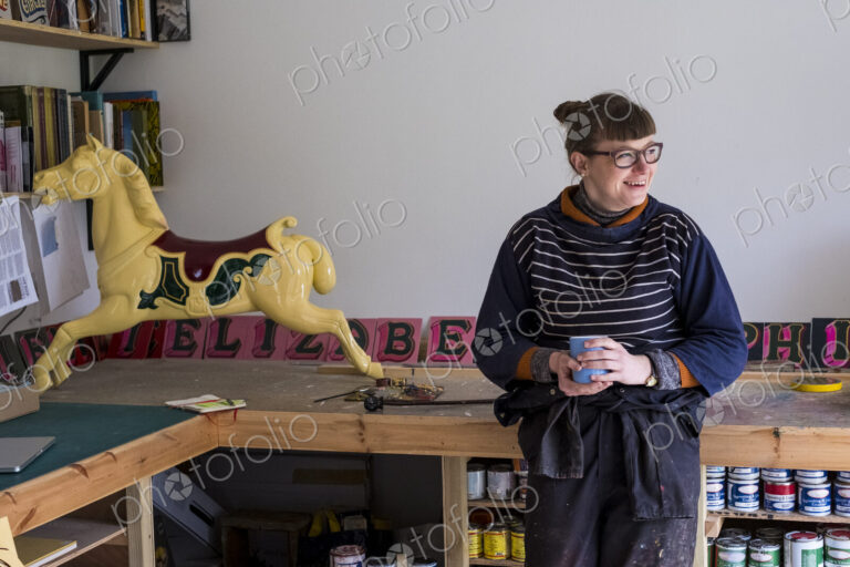 Woman in workshop next to traditional wooden carousel galloper horse from merry-go-round.