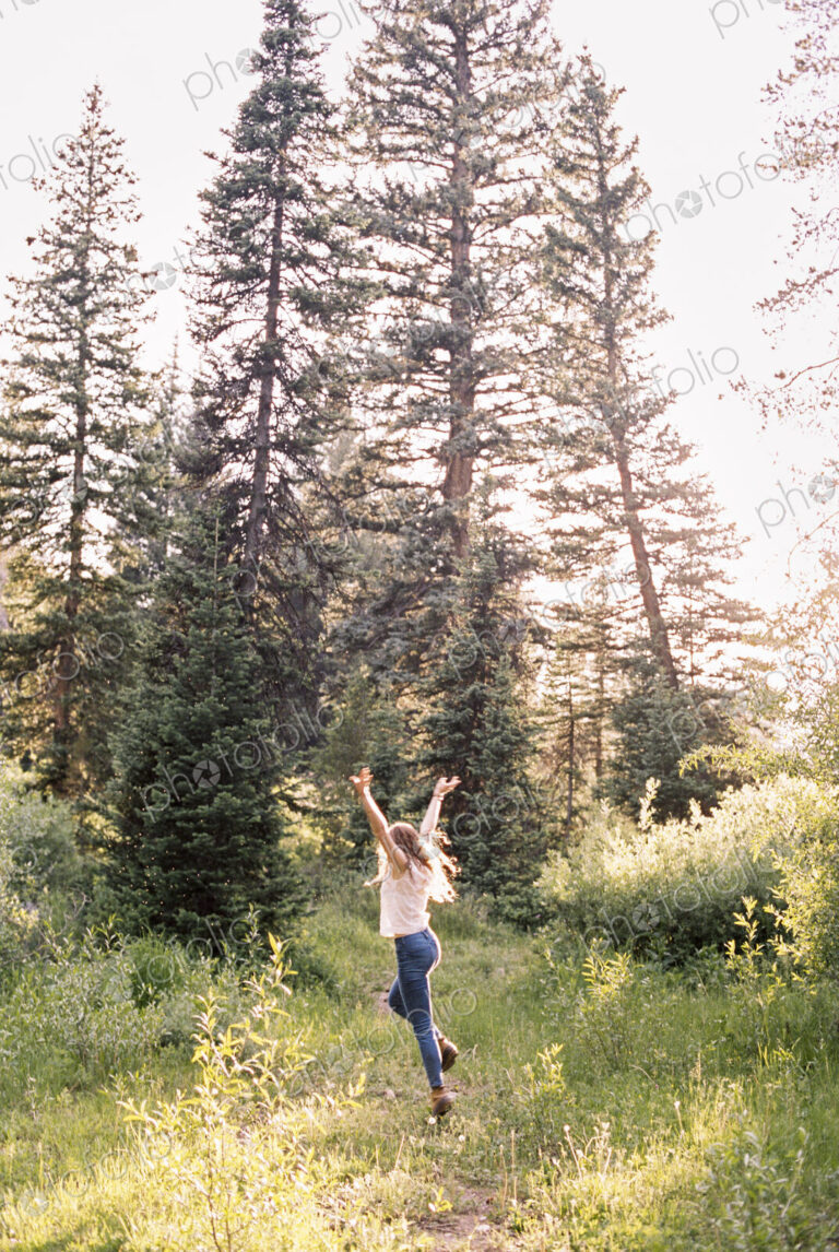 Woman jumping with joy in a sunlit forest.