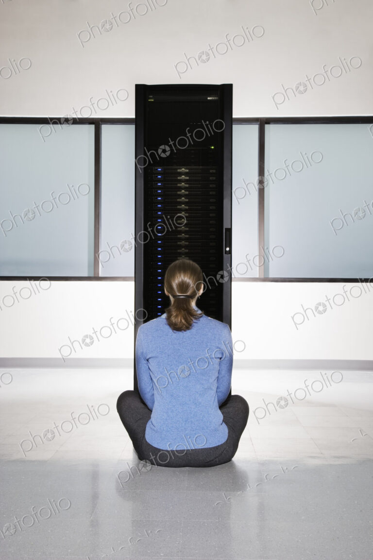 Woman lab technician sitting in front of a rack for servers in a computer server farm.