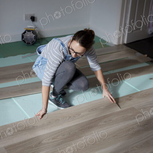 Woman laying new floorboards in the living room of a house under renovation. Woman laying new floorboards in the living room of a house under renovation.
