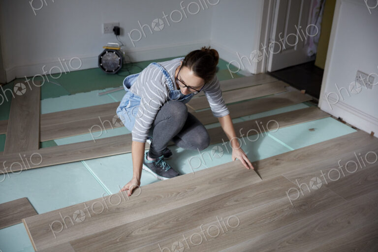 Woman laying new floorboards in the living room of a house under renovation.