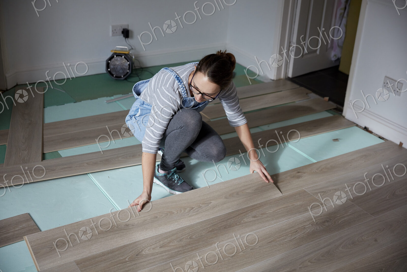 Woman laying new floorboards in the living room of a house under renovation.