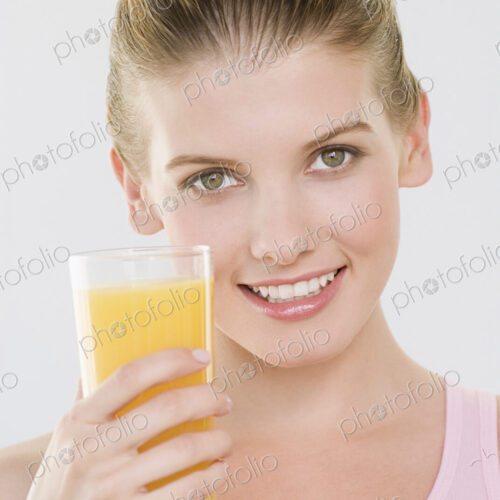 Woman looking at camera holding glass of orange juice.