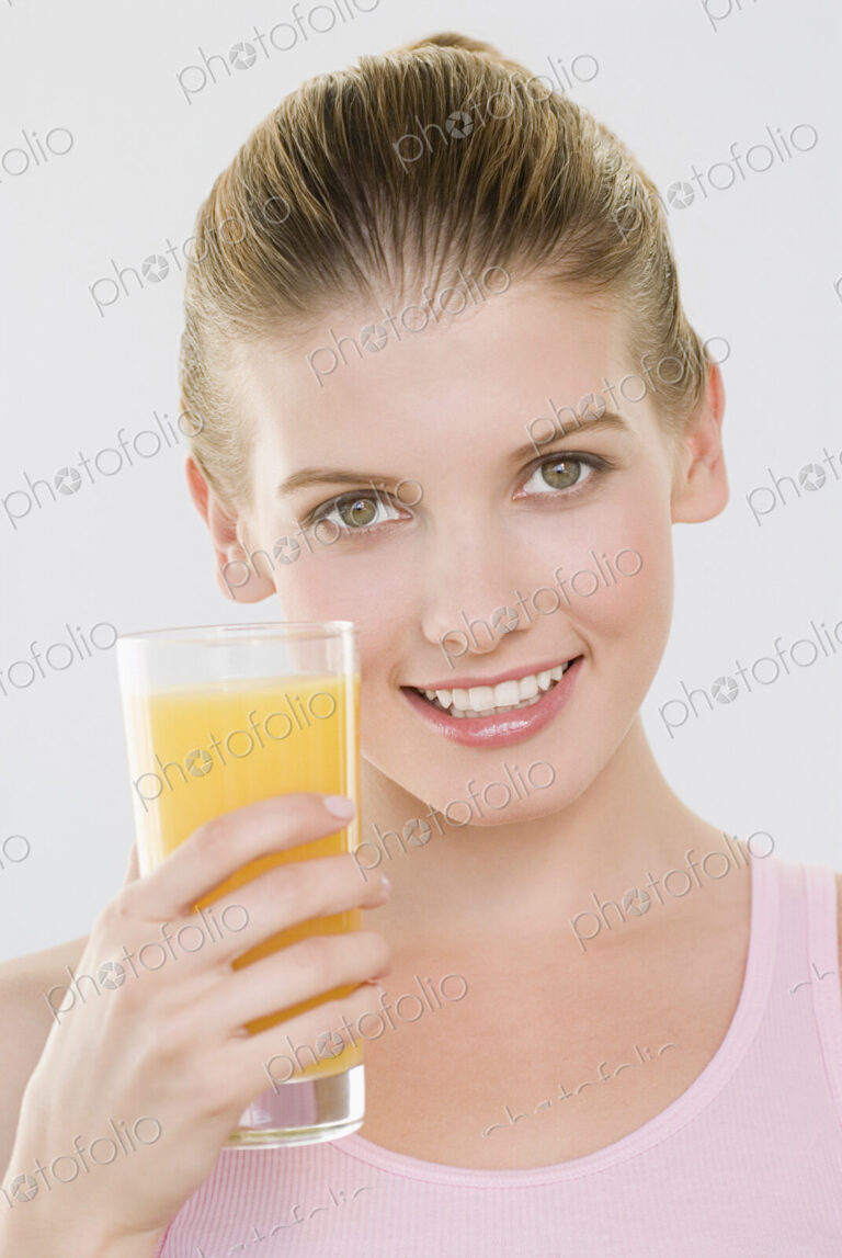 Woman looking at camera holding glass of orange juice.