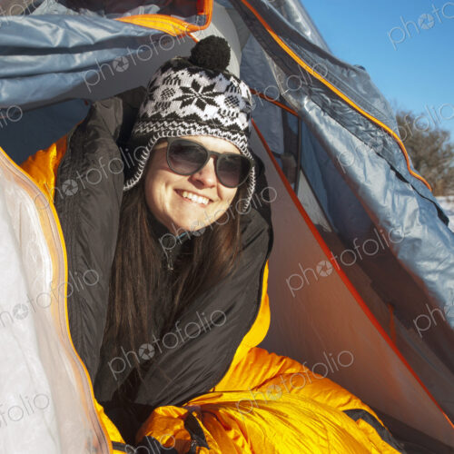 Woman looking out of tent flap smiling wearing winter hat. Woman looking out of tent flap smiling wearing winter hat.