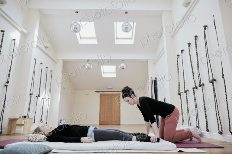 Woman lying down fully clothed having a Thai massage in a light filled exercise studio