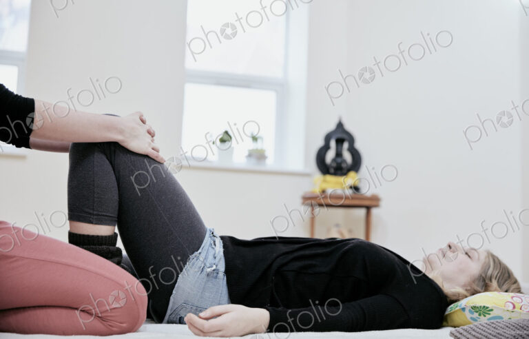 Woman lying down on her back and a Thai massage practioner gently stretching her knees…
