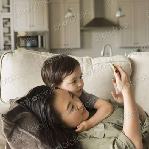 Woman lying on a sofa cuddling with her young son using a smart phone Woman lying on a sofa cuddling with her young son using a smart phone