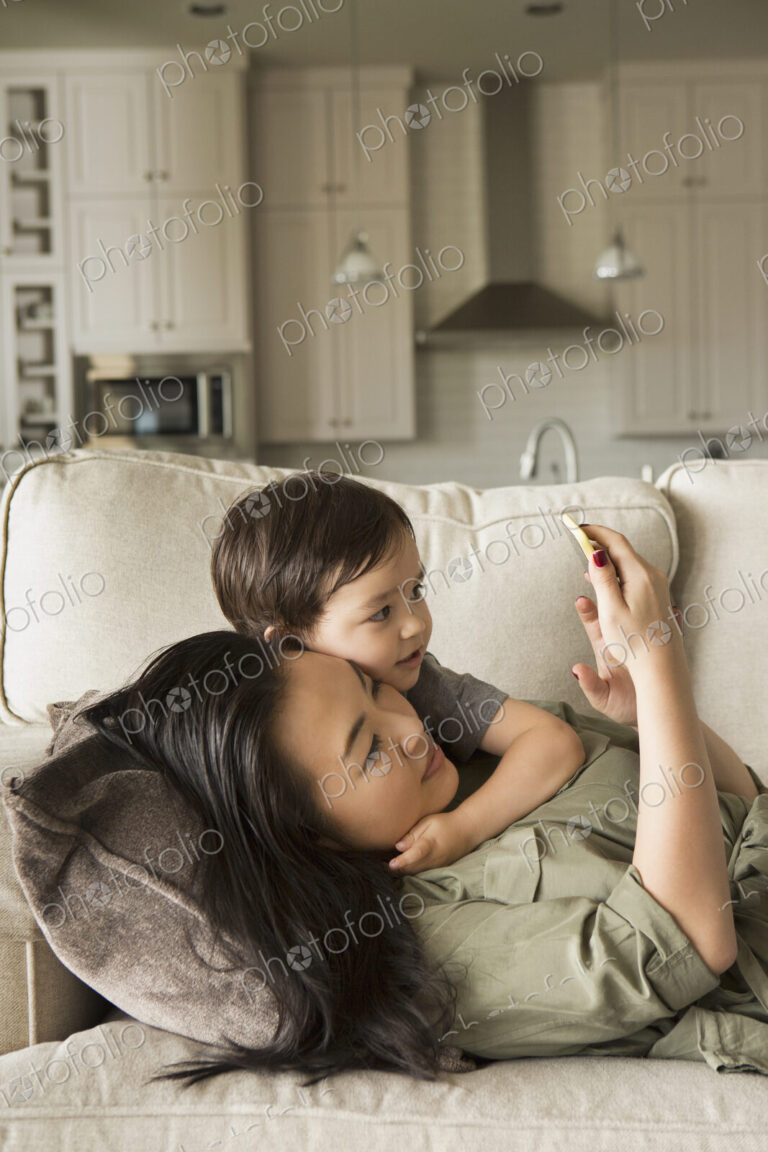 Woman lying on a sofa cuddling with her young son using a smart phone
