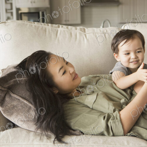 Woman lying on a sofa, smiling, cuddling with her young son and looking at a cell phone. Woman lying on a sofa, smiling, cuddling with her young son and looking at a cell phone.