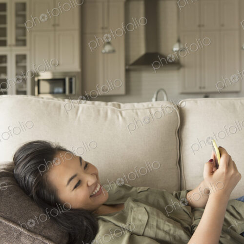 Woman lying on a sofa, smiling, looking at a cell phone. Woman lying on a sofa, smiling, looking at a cell phone.