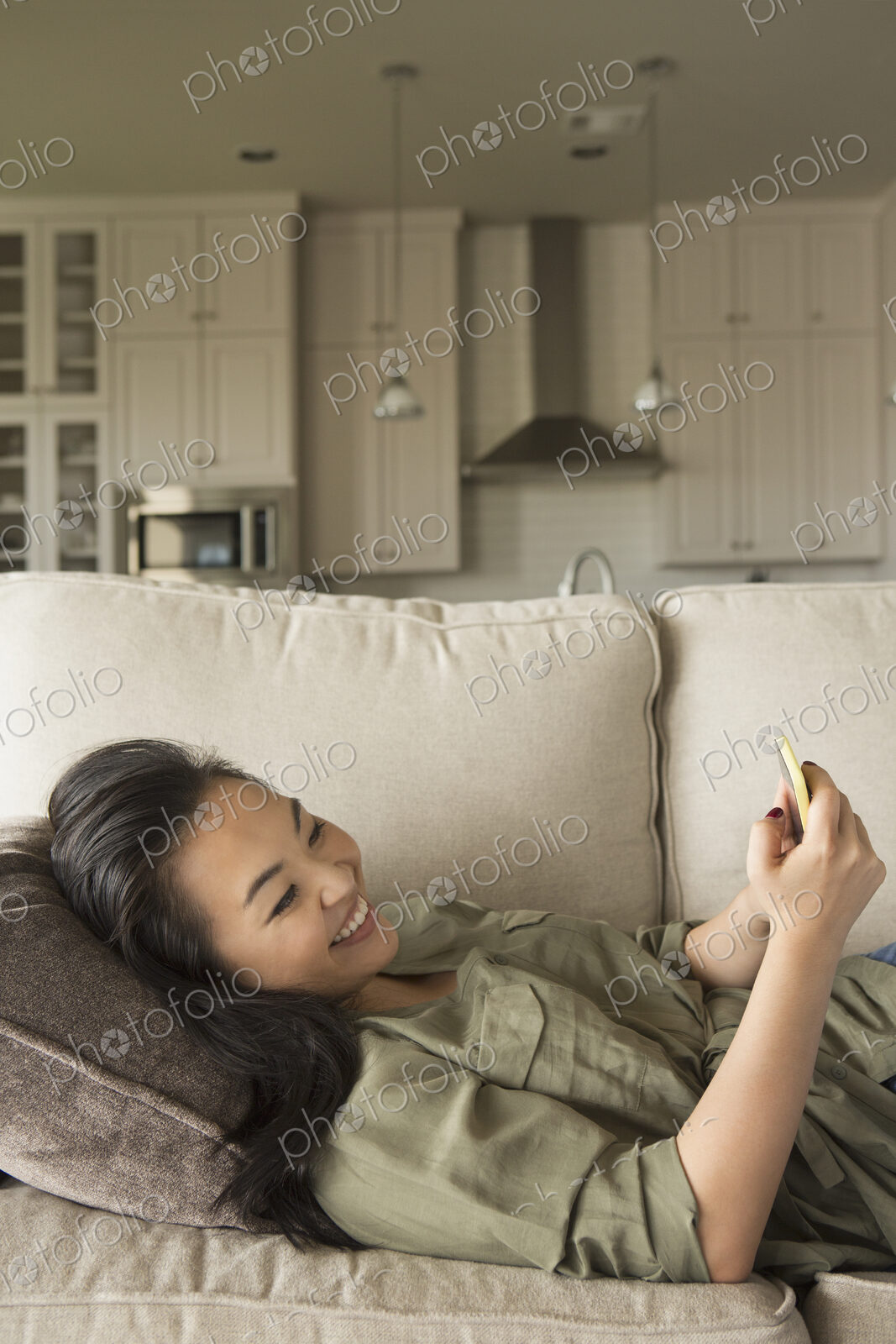 Woman lying on a sofa, smiling, looking at a cell phone.