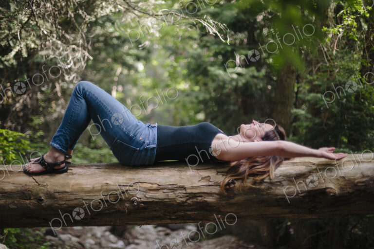 Woman lying on her back on a fallen tree trunk in a forest.