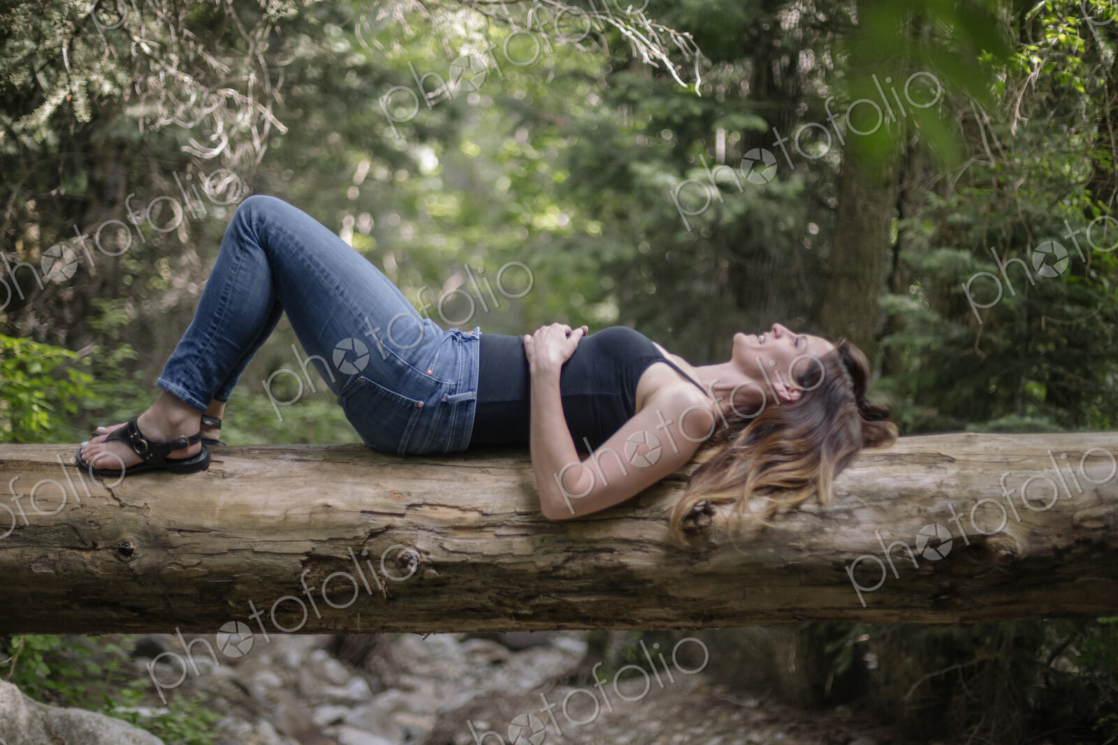 Woman lying on her back on a tree in a forest.