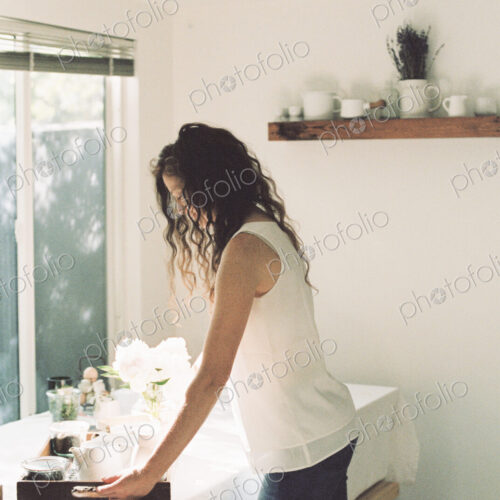 Woman placing a tray with a teapot and a vase of white roses on a table.