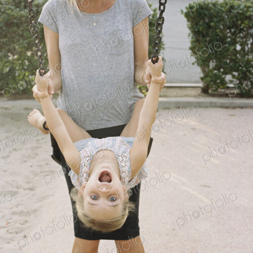 Woman playing with her daughter sitting on a swing.