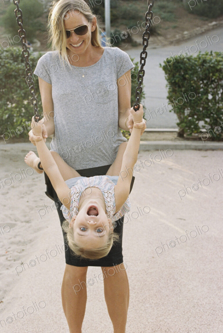 Woman playing with her daughter sitting on a swing.