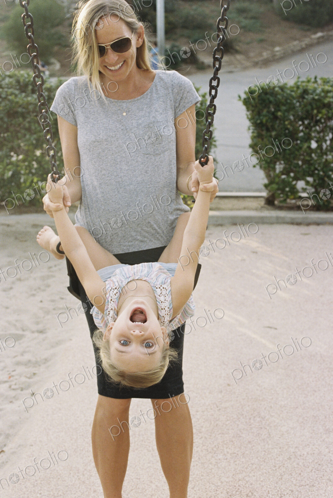 Woman playing with her daughter sitting on a swing.