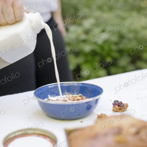 Woman pouring fresh milk into a bowl of cereal.