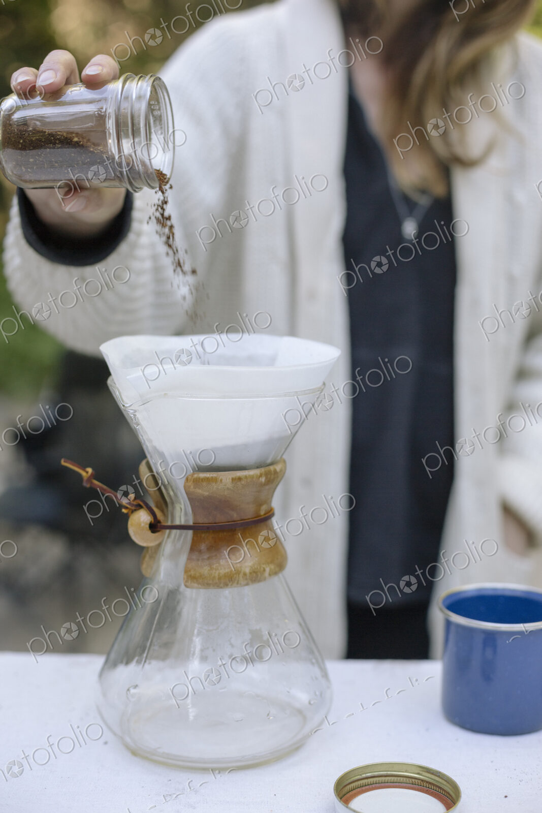 Woman pouring ground coffee from a jar into a glass coffee maker.