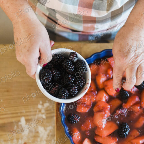 Woman pouring stewed fruit into a pie dish. Fresh blackberries.