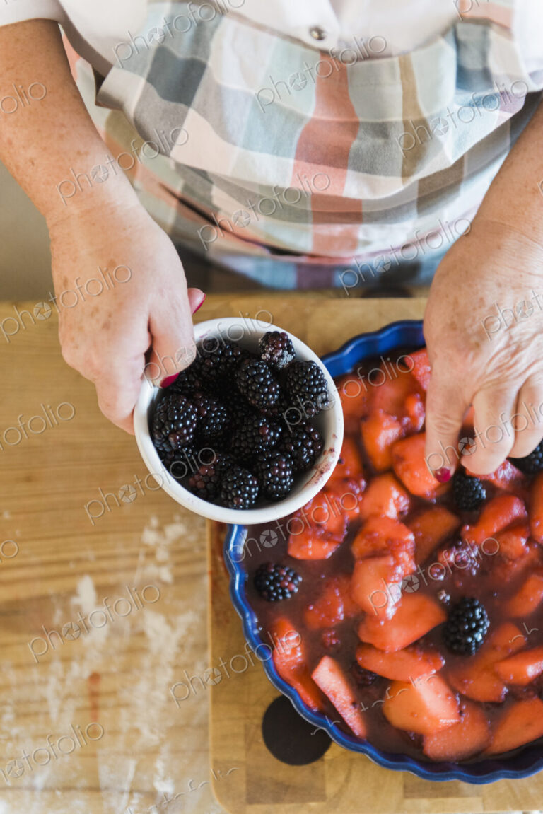 Woman pouring stewed fruit into a pie dish. Fresh blackberries.