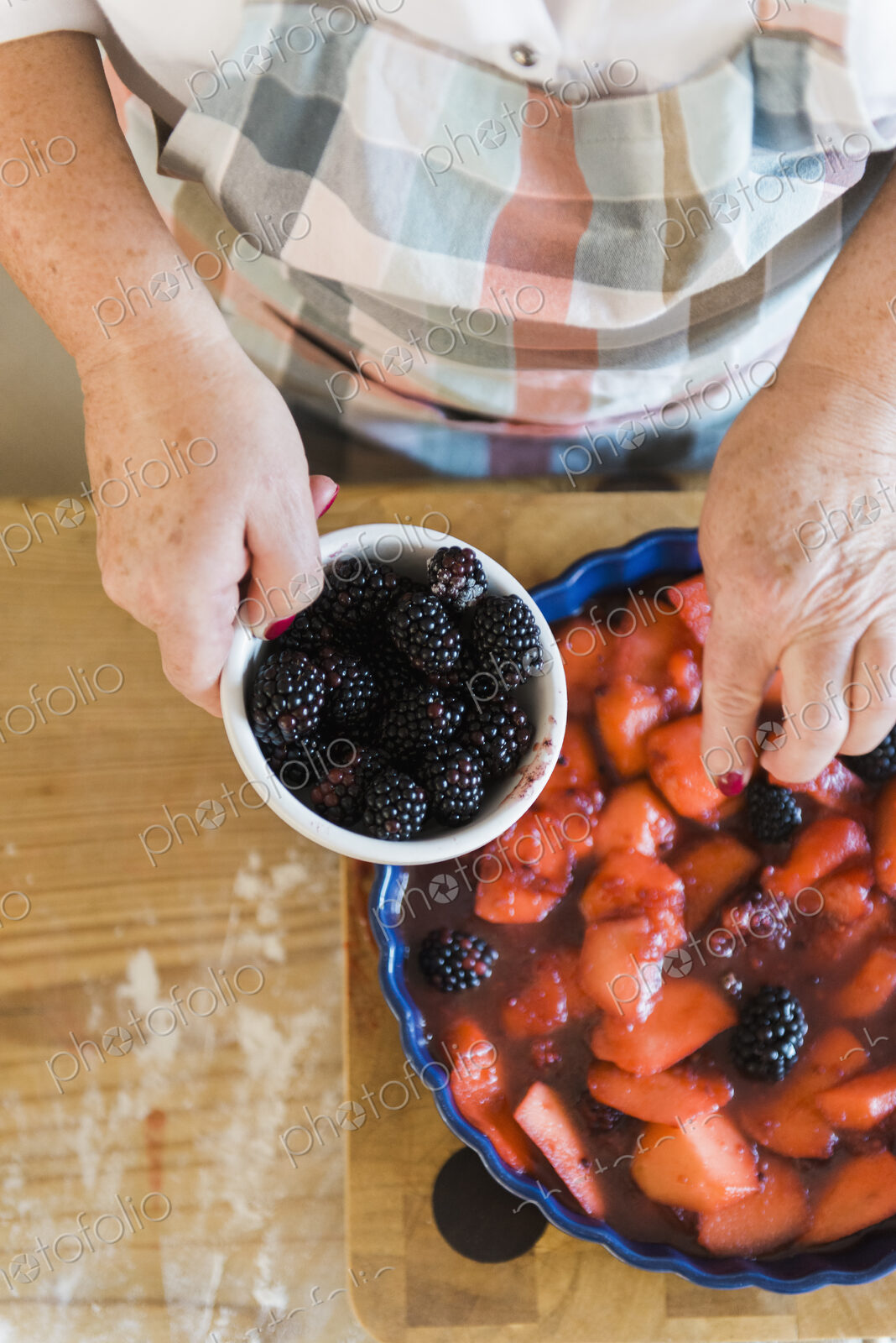 Woman pouring stewed fruit into a pie dish. Fresh blackberries.
