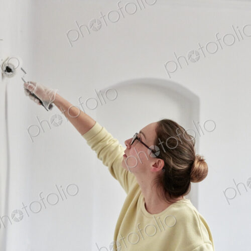 Woman reaching up using roller to paint wall Woman reaching up using roller to paint wall