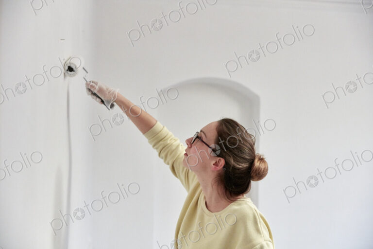 Woman reaching up using roller to paint wall