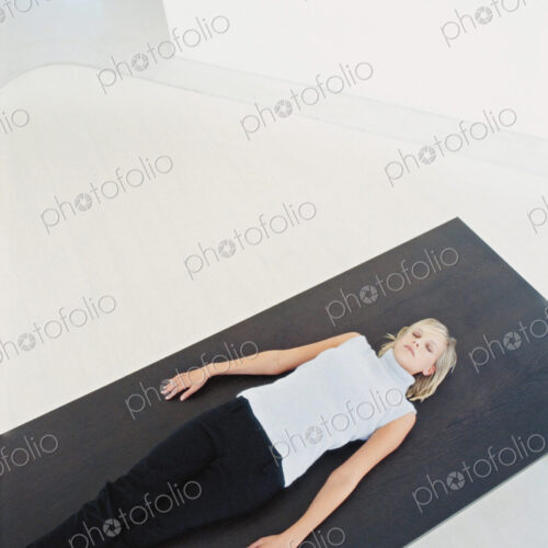 Woman reclining on yoga mat in white modern space.