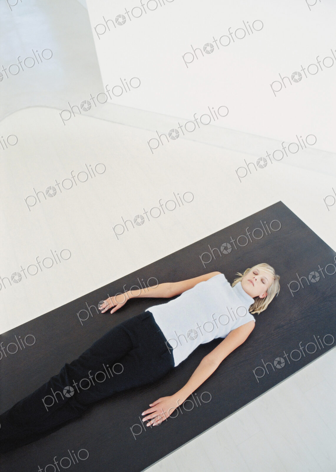 Woman reclining on yoga mat in white modern space.
