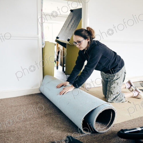 Woman rolling up old carpet in preparation to renew flooring Woman rolling up old carpet in preparation to renew flooring