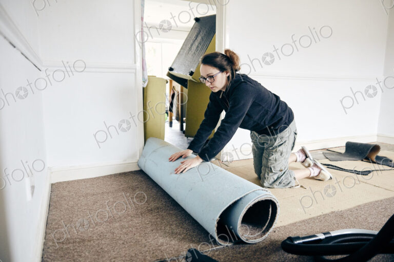 Woman rolling up old carpet in preparation to renew flooring