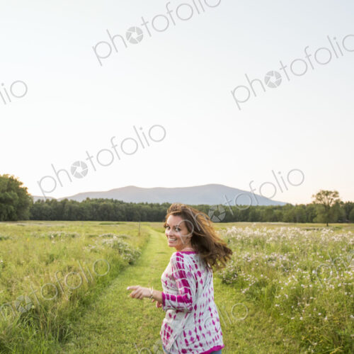 Woman running along a path in a meadow, looking over her shoulder. Woman running along a path in a meadow, looking over her shoulder.
