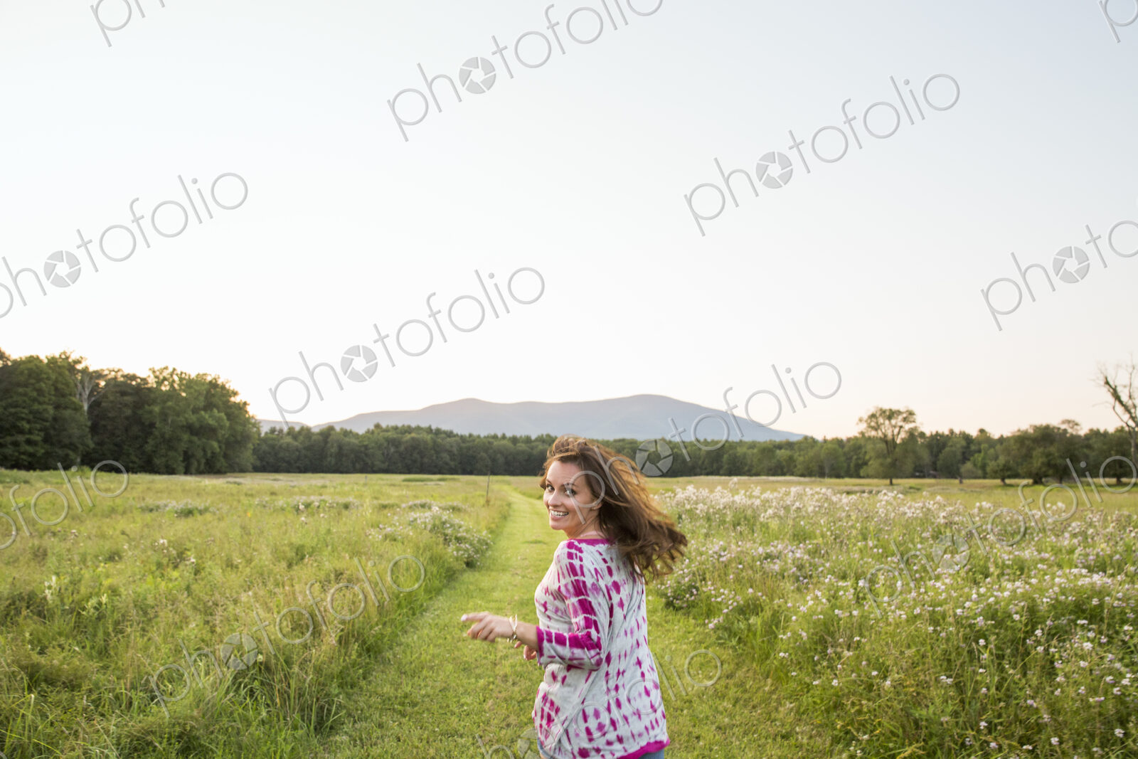 Woman running along a path in a meadow, looking over her shoulder.