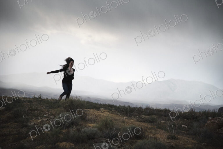 Woman running in a prairie under a cloudy sky.