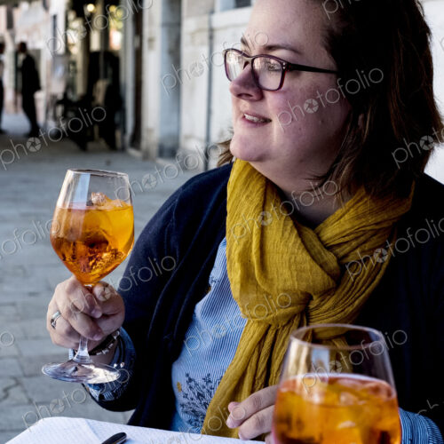Woman seated at a table outdoors, holding a glass of Aperol Spritz