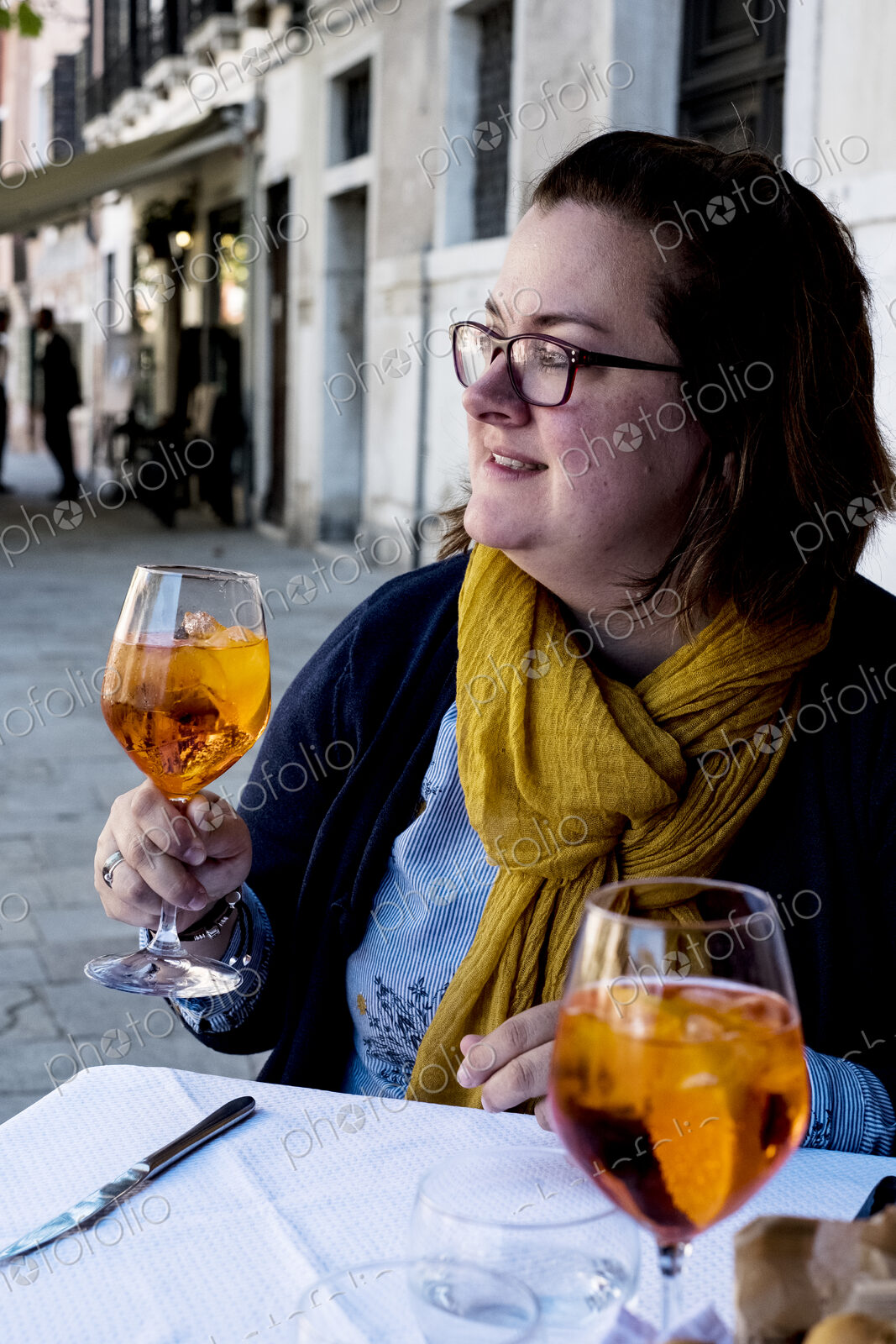 Woman seated at a table outdoors, holding a glass of Aperol Spritz