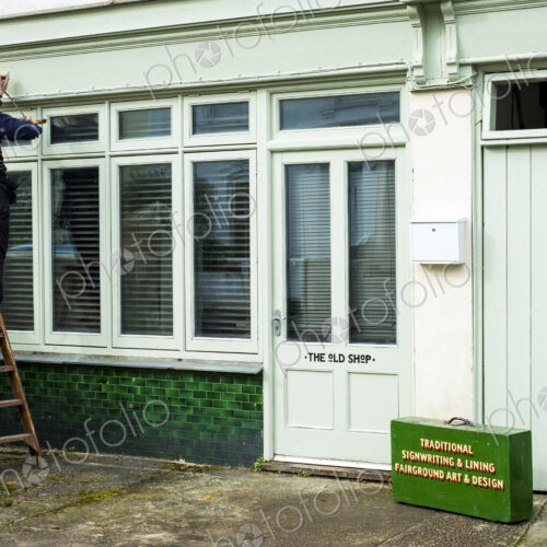 Woman sign writer standing on a ladder using paintbrush and maulstick Woman sign writer standing on a ladder using paintbrush and maulstick