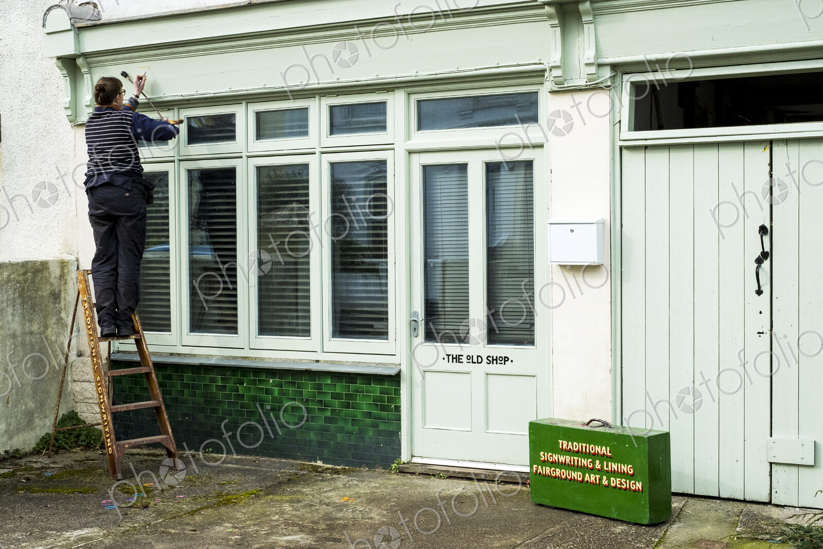Woman sign writer standing on a ladder using paintbrush and maulstick