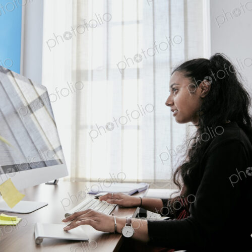 Woman sitting at a desk in an office using a computer keyboard and looking at a screen.