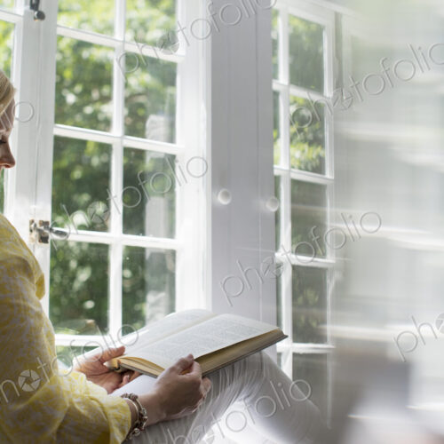 Woman sitting by a window, reading a book. Woman sitting by a window, reading a book.