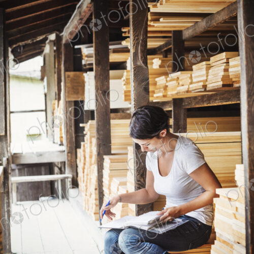 Woman sitting in a lumber yard, holding a folder.