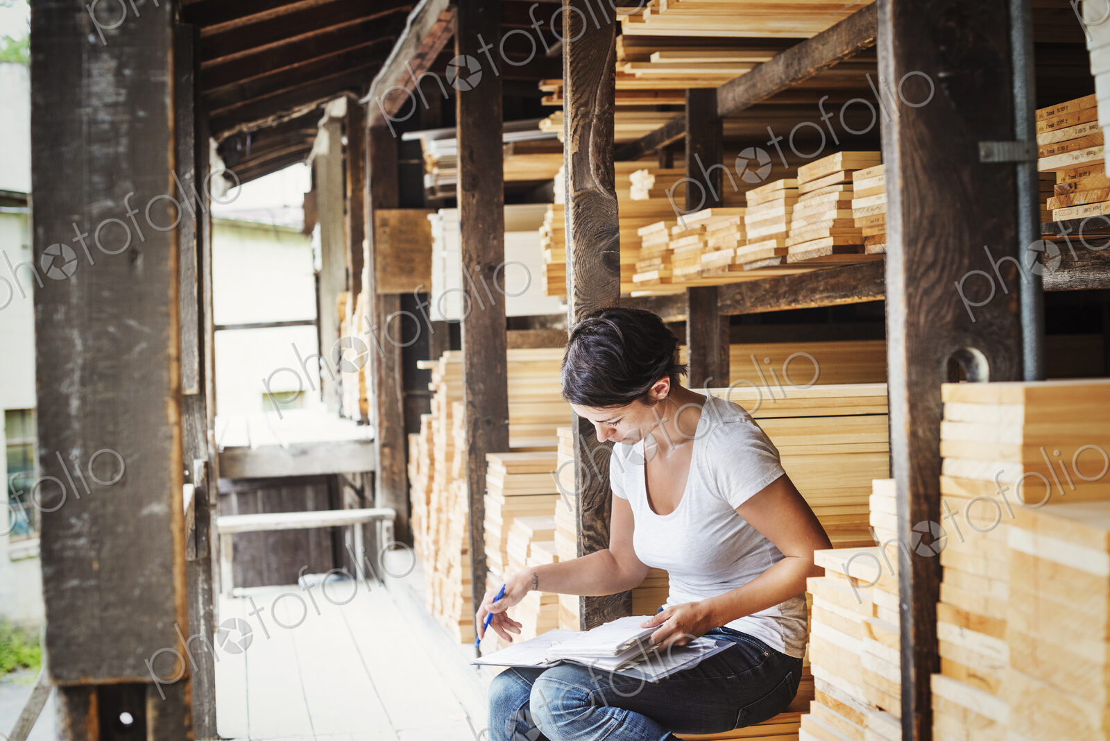 Woman sitting in a lumber yard, holding a folder.