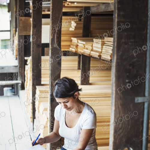 Woman sitting in a lumber yard, holding a folder.