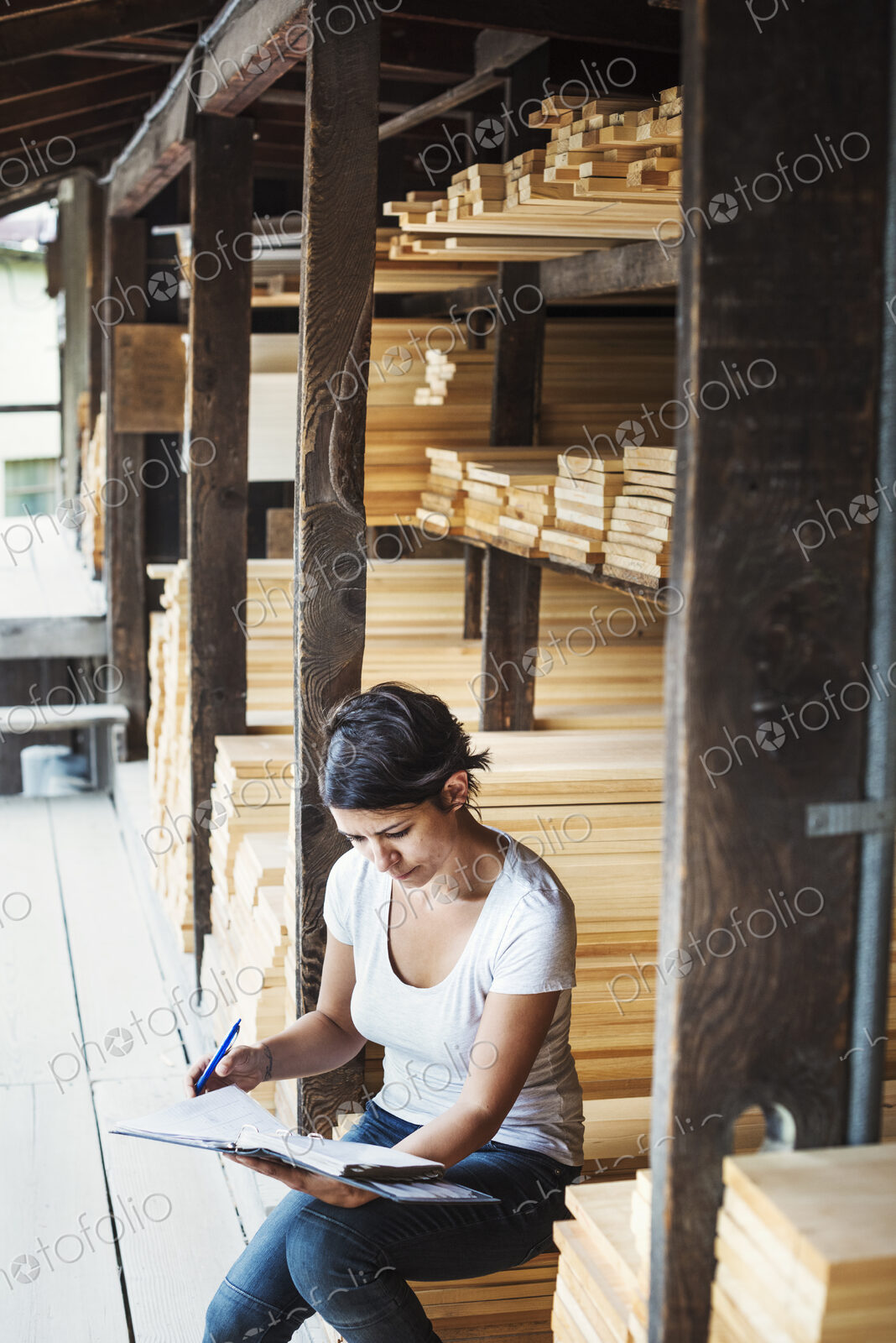 Woman sitting in a lumber yard, holding a folder.