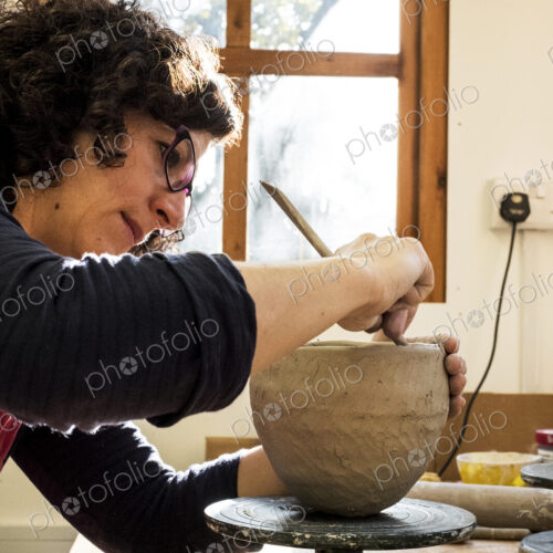 Woman sitting in her ceramics workshop, working on clay vase.