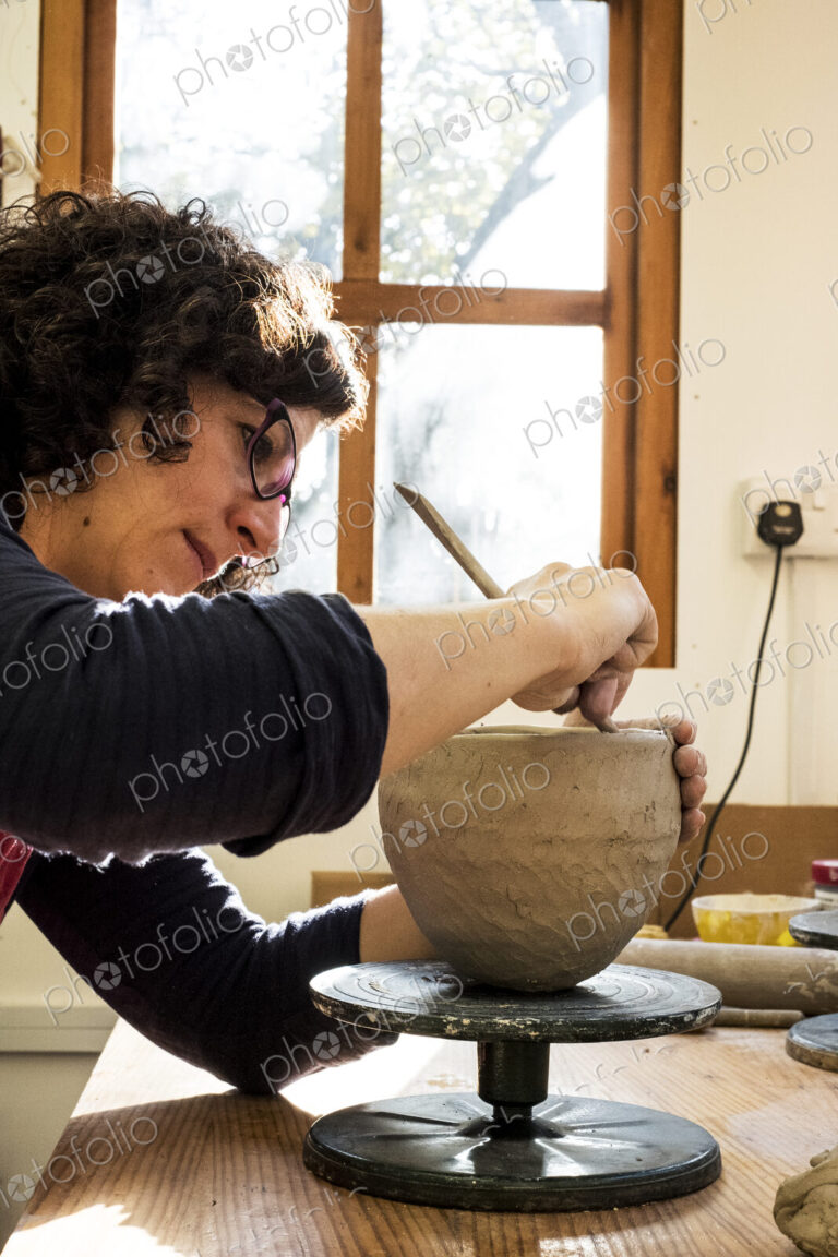 Woman sitting in her ceramics workshop, working on clay vase.